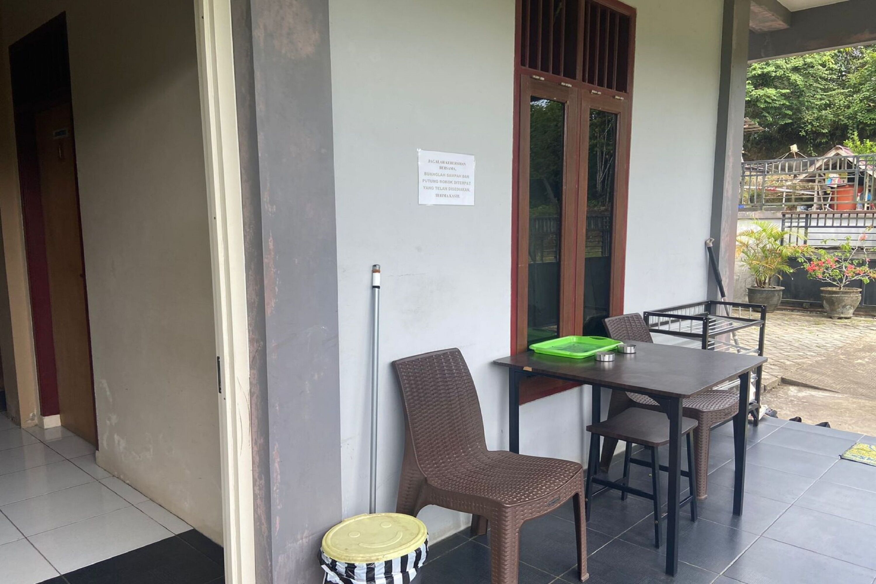A covered outdoor seating area with a table and chairs, a trash bin, and a sign on the wall.