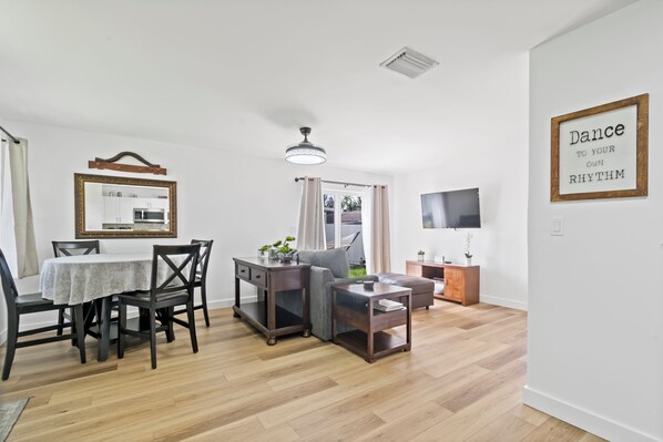 A modern living room with a dining area, a TV, and a motivational quote on the wall.