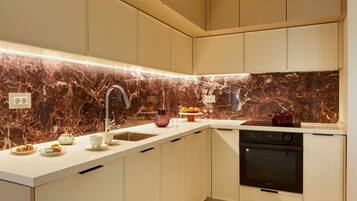A modern kitchen with white cabinets, a marble backsplash, a stainless steel sink, and a built-in oven.