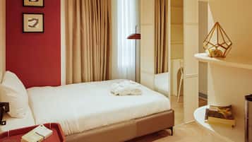 A modern hotel room with a large bed, a red cabinet, a desk with a lamp, and a bookshelf.