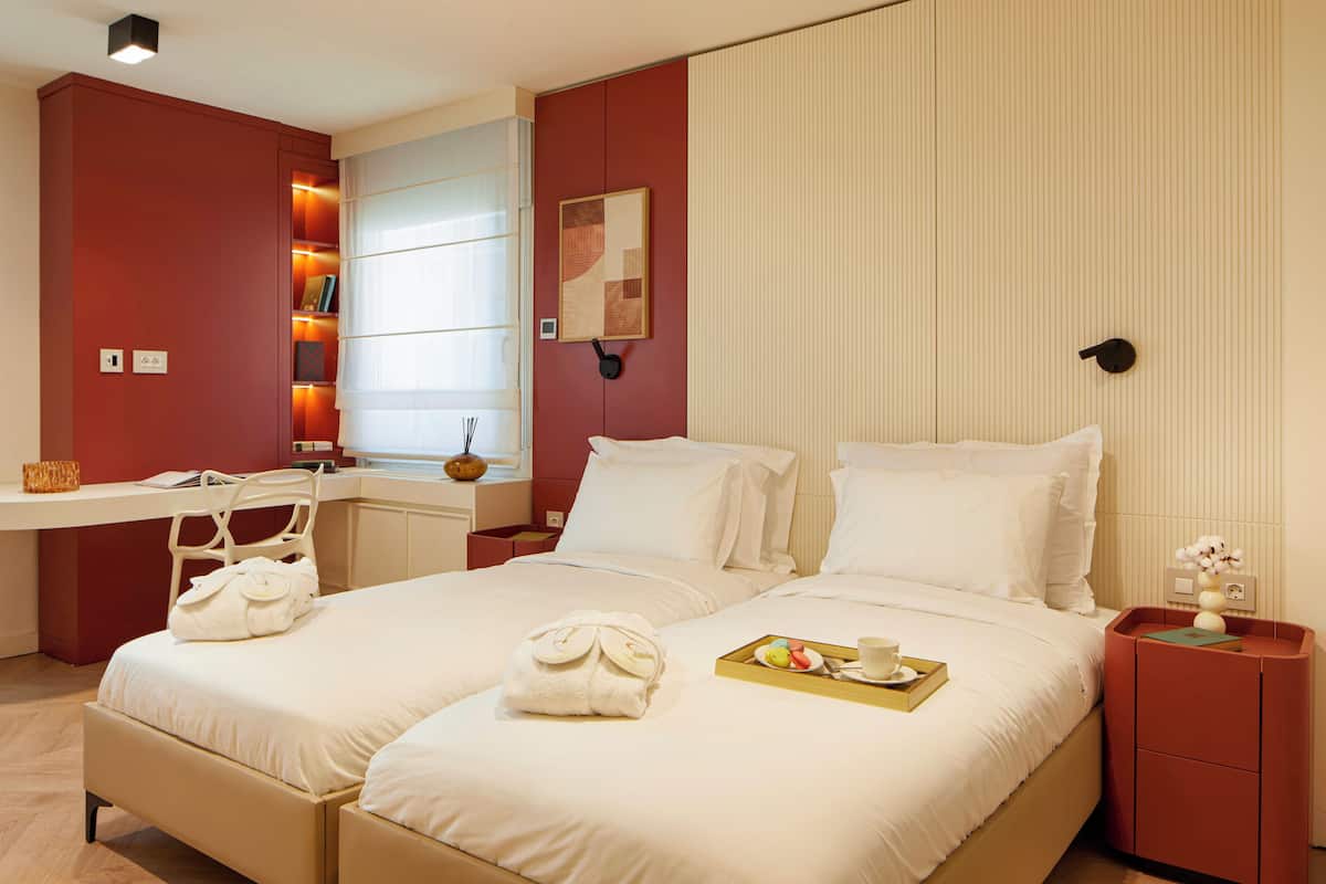 A hotel room with two beds, a desk, and a bookshelf.