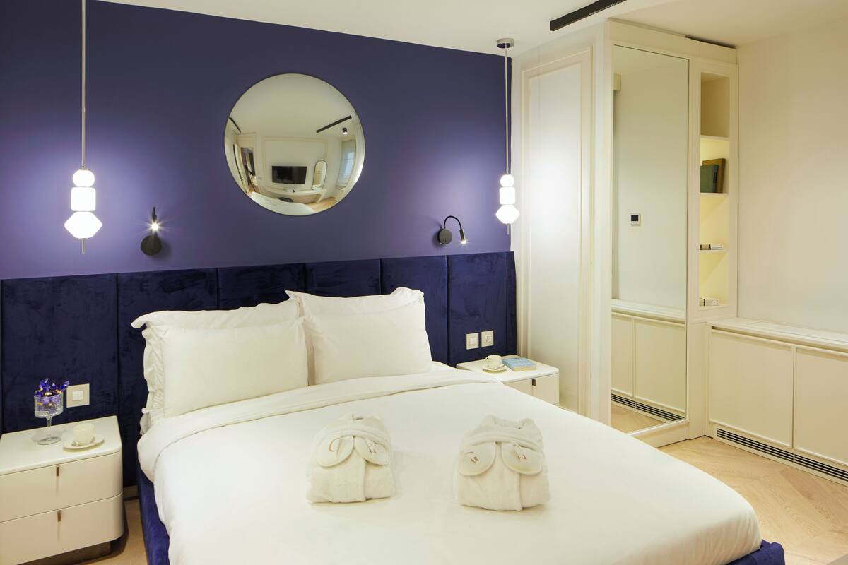 A modern hotel room with a large bed, bedside tables, a mirror, and a wardrobe.