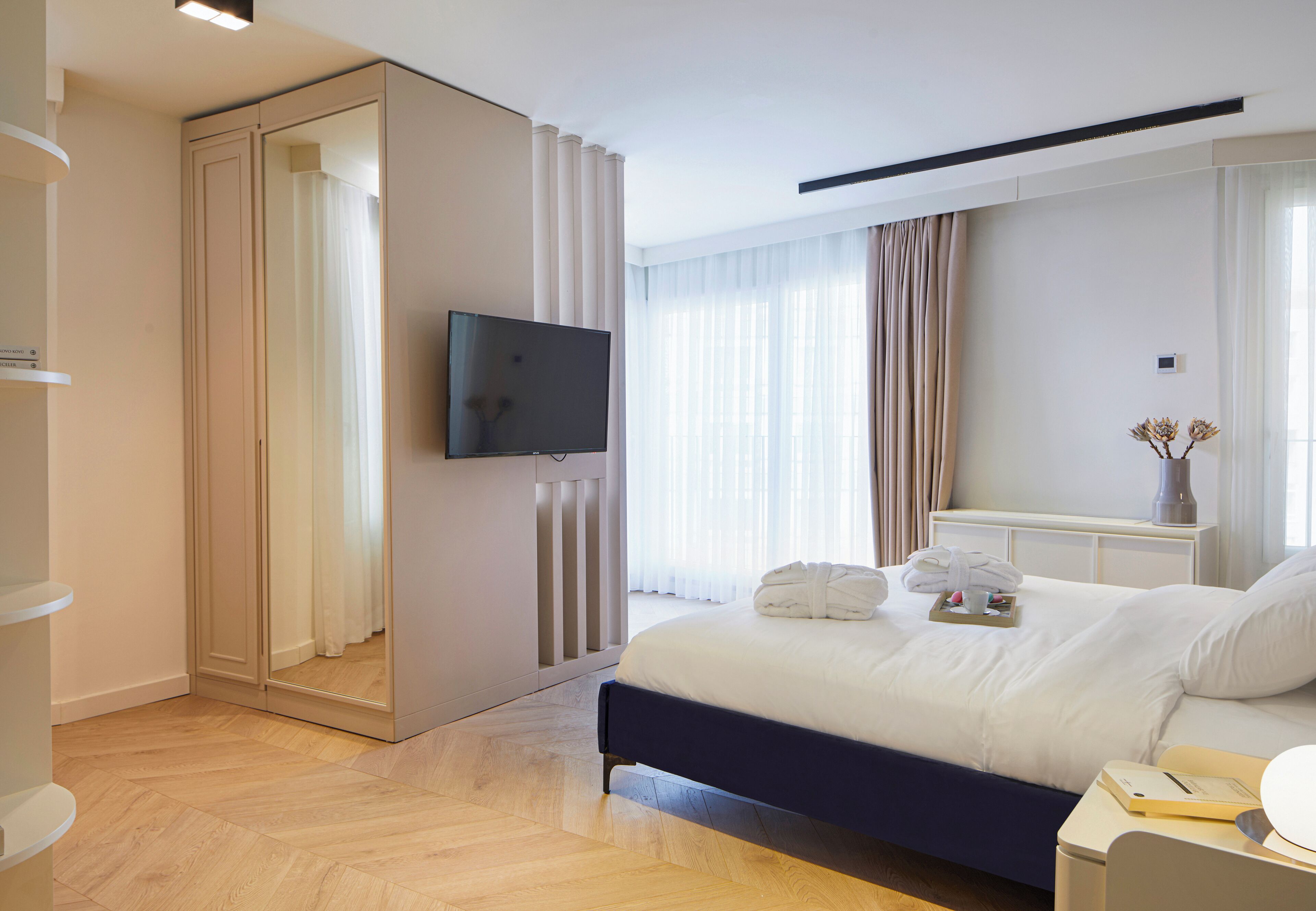 Une chambre d’hôtel moderne dotée d’un grand lit, d’un téléviseur à écran plat, d’une table de chevet avec une lampe et offrant une vue sur la ville grâce à de grandes fenêtres.