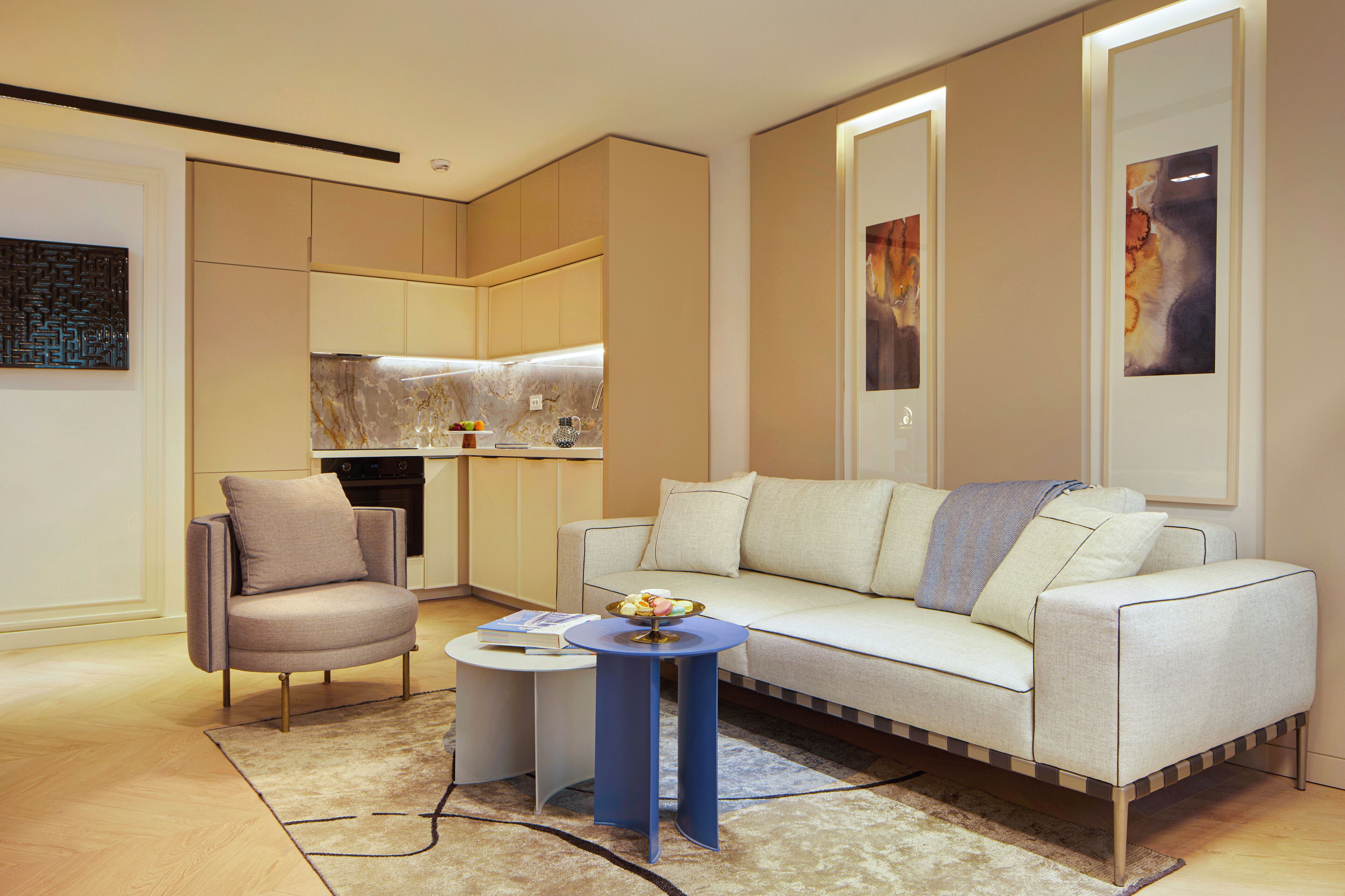 Una sala de estar moderna con un sofá, una silla, una mesita y una zona de cocina al fondo.
