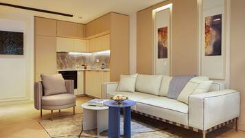 Una sala de estar moderna con un sofá, una silla, una mesita y una zona de cocina al fondo.