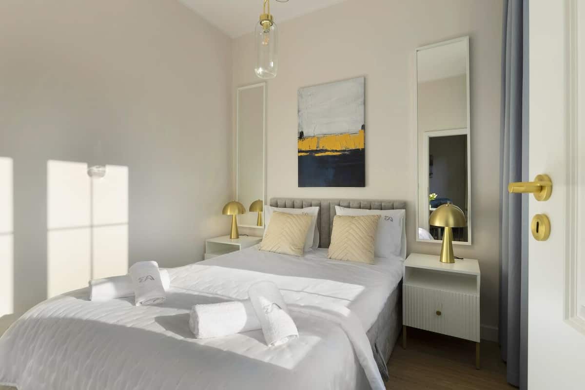 A neatly made bed with white linens and towels, a bedside lamp, and a painting on the wall.