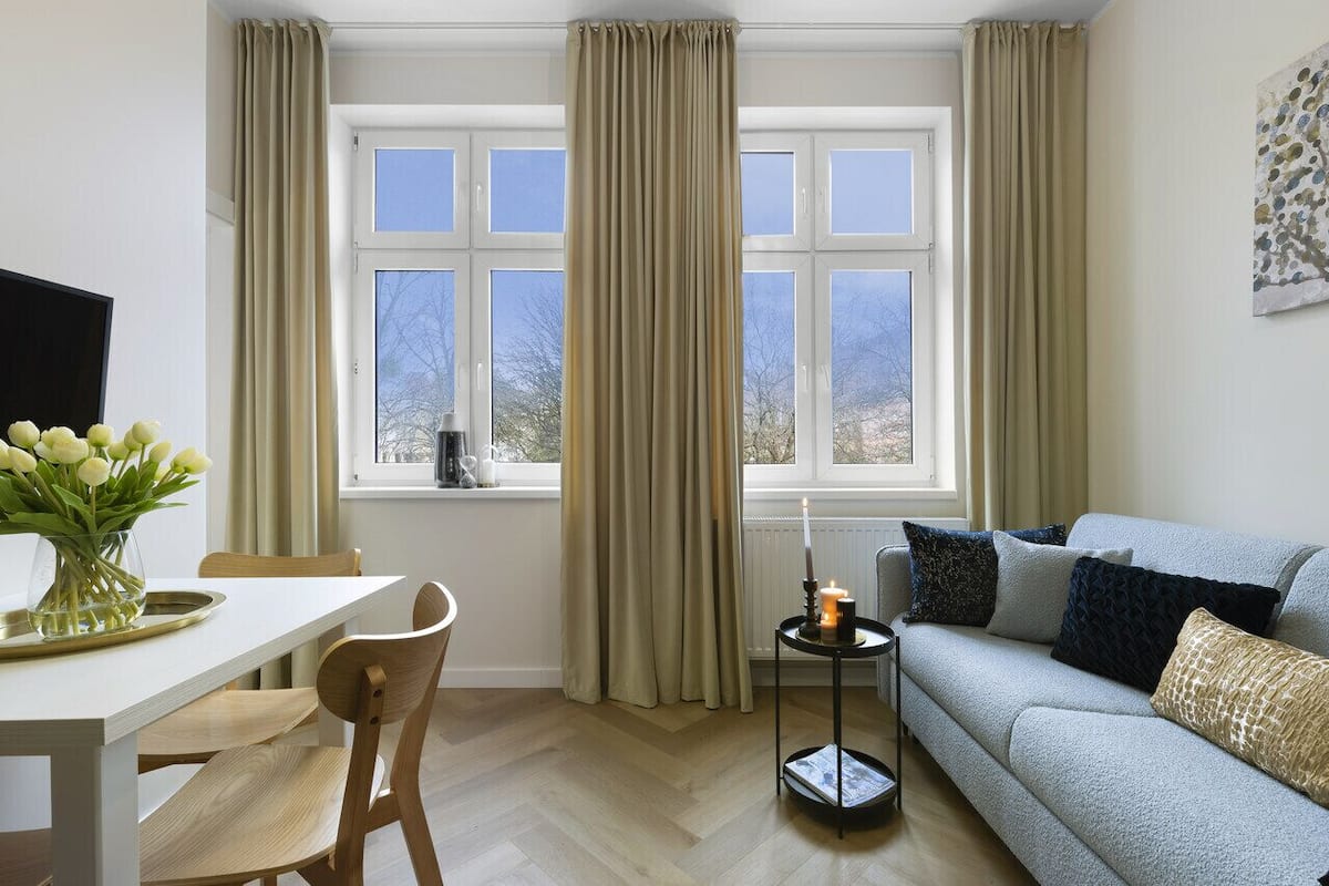 A modern living room with a sofa, a dining table with chairs, and a window with curtains.