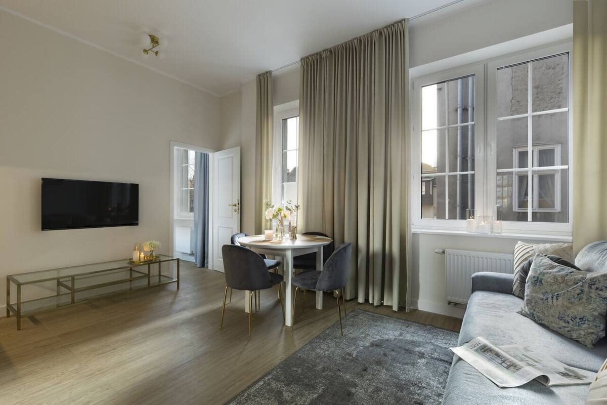 A modern living room with a flat-screen TV, a dining table with chairs, a sofa, and a window with curtains.
