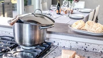 A kitchen with a stove, a pot on the burner, a cutting board with cheese, and a bottle of wine on the counter.