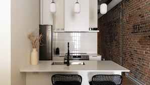 A modern kitchen with a white island, black chairs, a stainless steel refrigerator, and a brick wall.