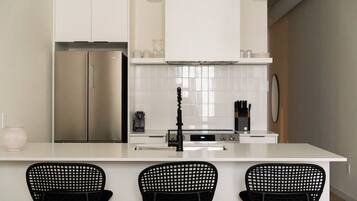 Cocina moderna con armarios blancos, un refrigerador de acero inoxidable, un grifo negro y tres sillas negras en la isla.