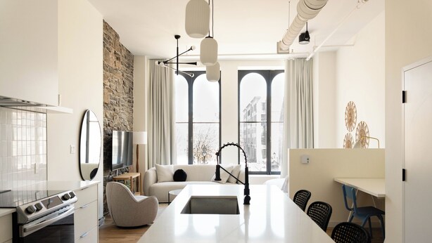 A modern kitchen with a central island, a dining area with chairs, and large windows with a view of buildings.