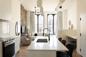 Una cocina moderna con una isla central, un área de comedor con sillas y ventanas amplias con vistas a edificios.