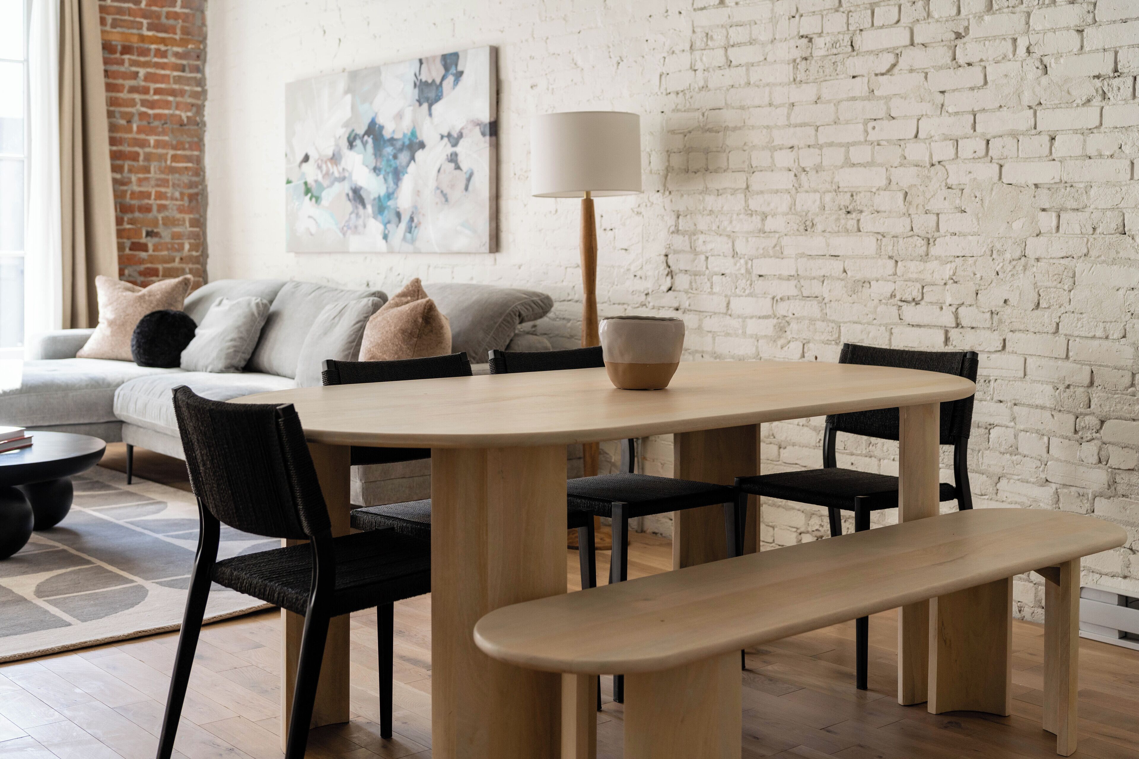 Un coin repas comprenant une table ronde, quatre chaises, un banc et une lampe.