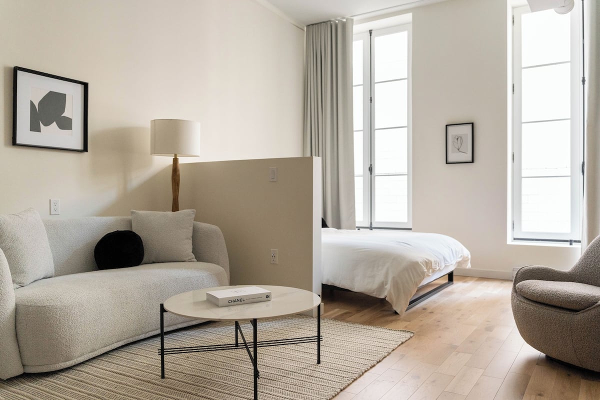 A modern, well-lit room with a sofa, a small round table, a bed, and a chair.
