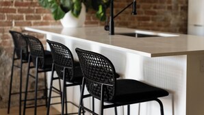 A kitchen with a white countertop, black chairs, and a black faucet.