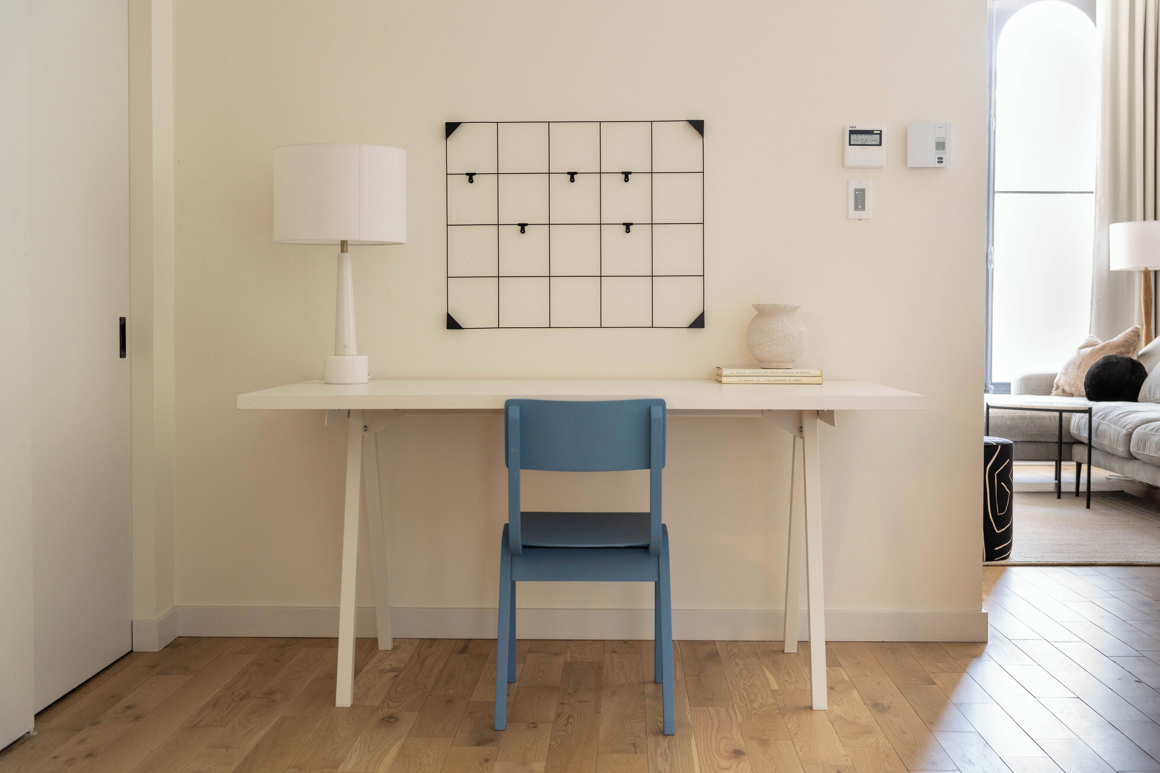 Una habitación moderna con un escritorio blanco, una silla azul, una lámpara blanca y un interruptor de luz en la pared.