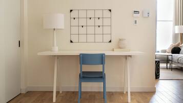 Una habitación moderna con un escritorio blanco, una silla azul, una lámpara blanca y un interruptor de luz en la pared.