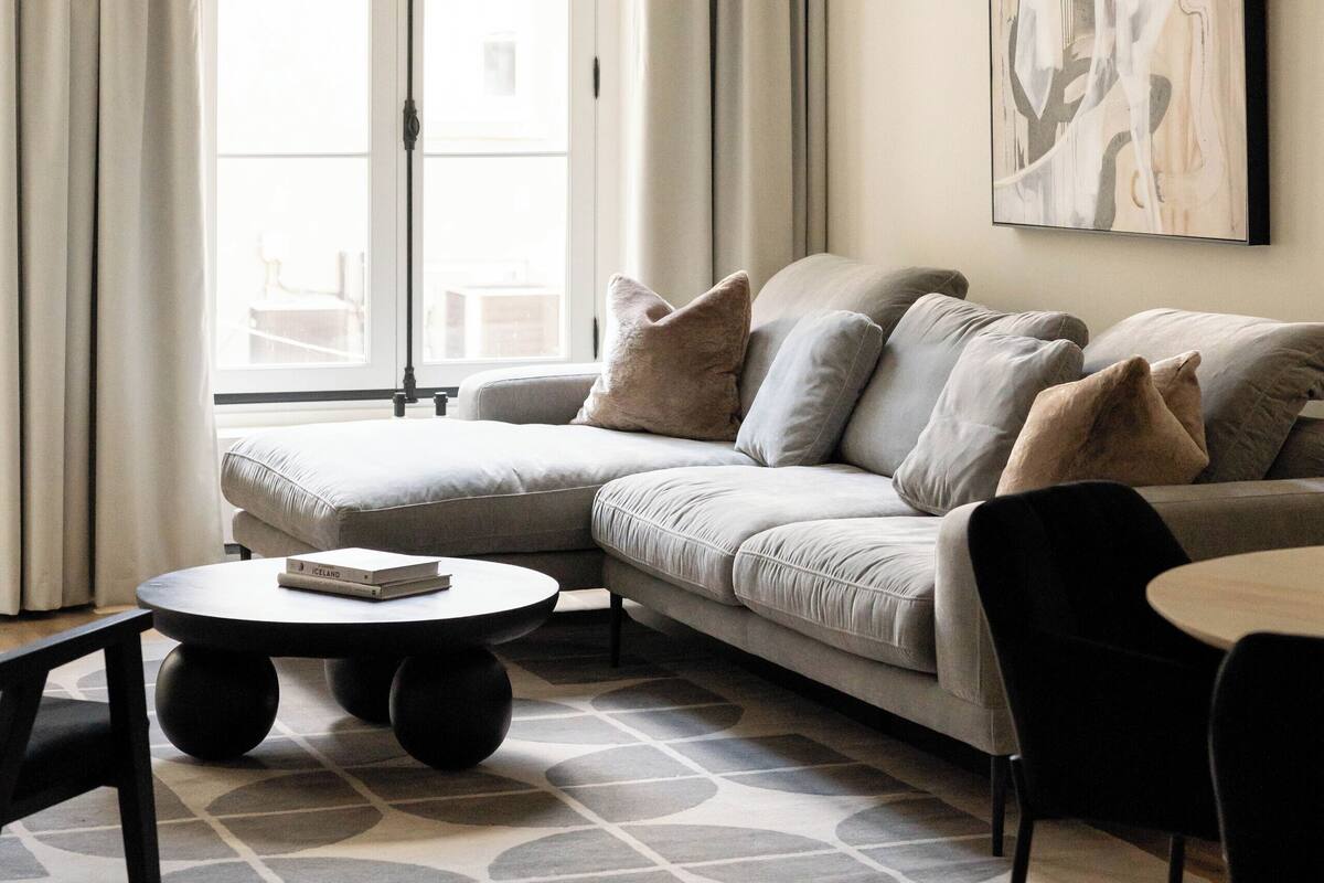 A modern living room with a sectional sofa, a round coffee table, and a dining area with a small table and chairs.