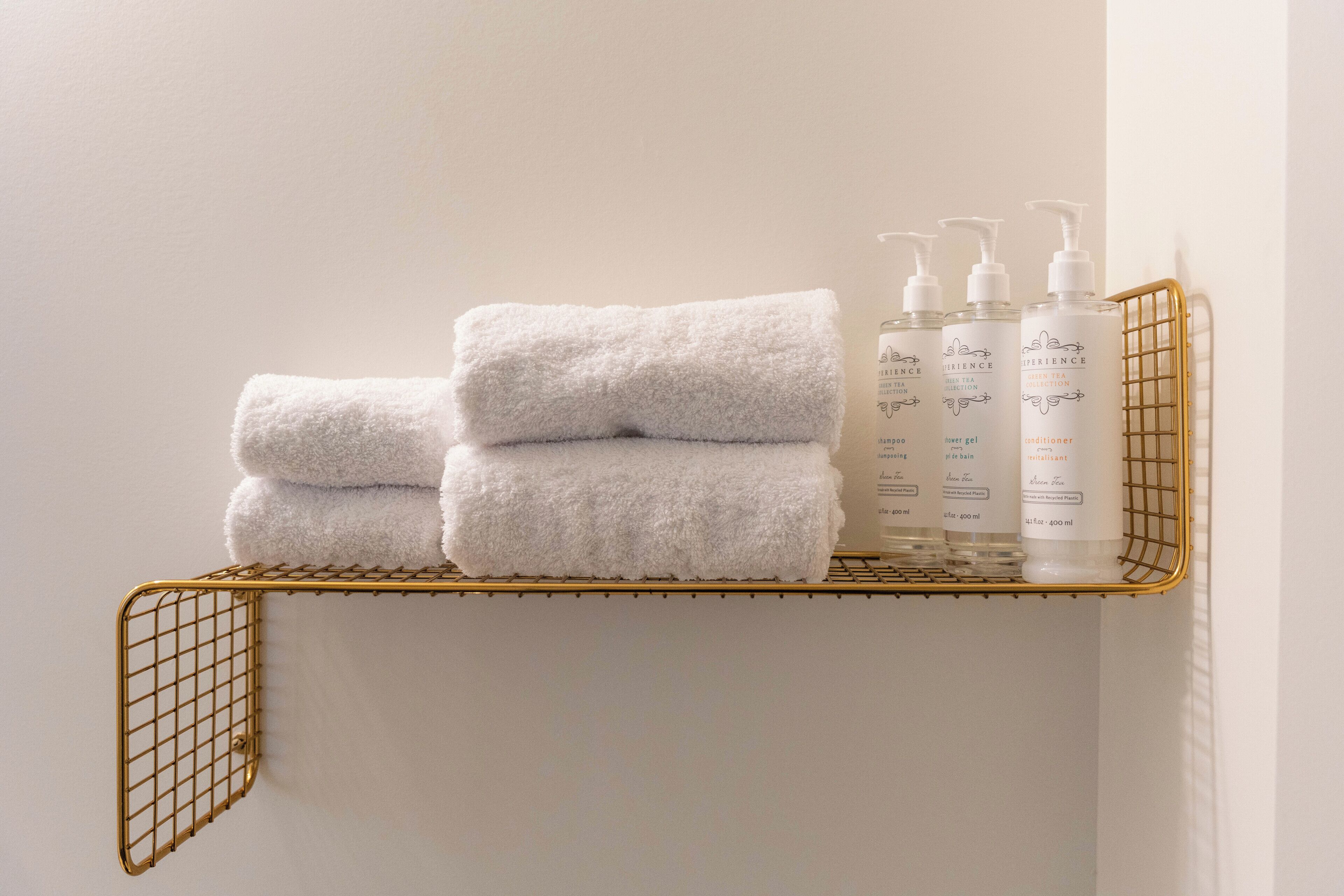 A white towel folded on a gold wire shelf, with three bottles of skincare products beside it.