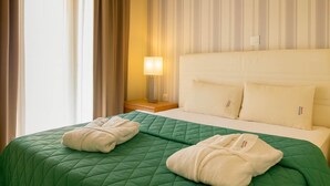 Ein Hotelzimmer mit einer grün gesteppten Bettdecke, zwei Kissen, einer Nachttischlampe und einem Fenster mit Vorhängen.
