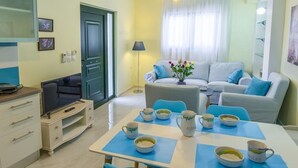 Ein modernes Wohnzimmer mit Sofa, Couchtisch und Esstisch mit Stühlen. Im Raum befindet sich ein Fernseher und ein Schrank.