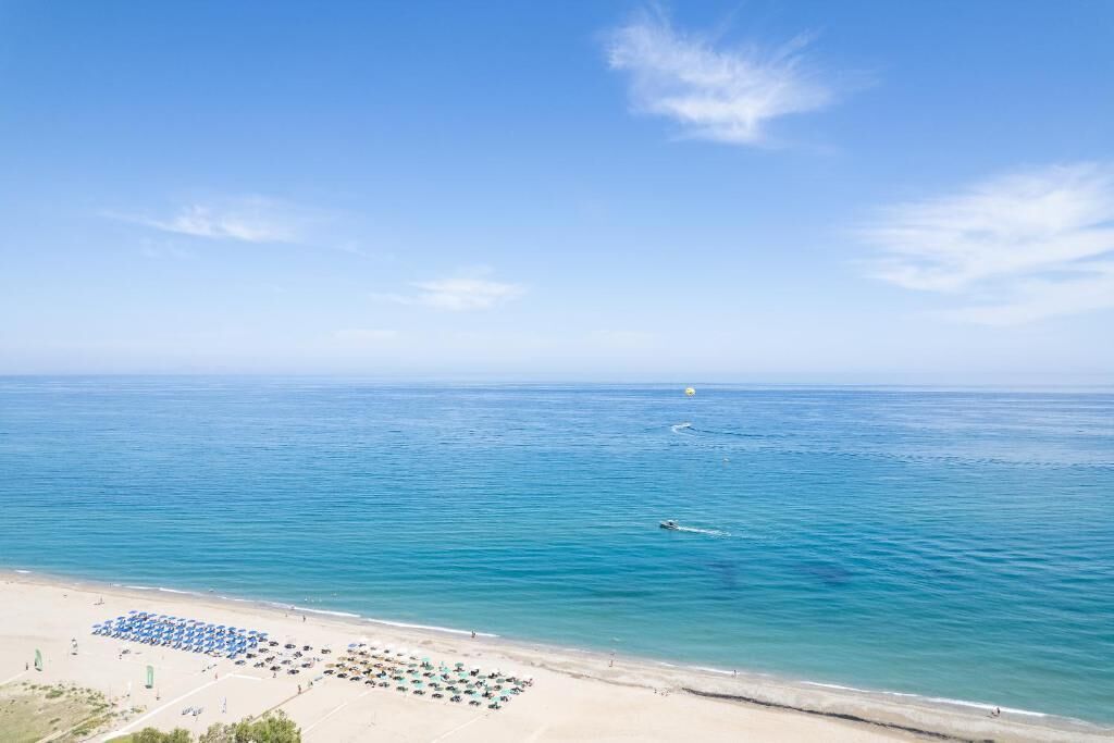 A beach with clear blue water, a sandy shore, and umbrellas.