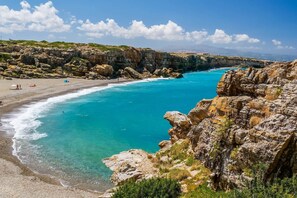 Eine Küstenlandschaft mit Strand, felsigen Klippen und klarem türkisblauem Wasser.