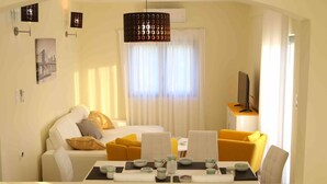 Una habitación de hotel con cama, sofá, mesa de comedor y tazas de té, y un televisor sobre un mueble.