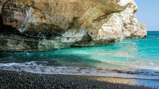 Una costa rocosa con aguas turquesas cristalinas y una playa de guijarros.