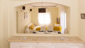 Habitación de hotel compacta con pared espejada, una kitchenette pequeña, zona de comedor con mesa y sillas, y cama con almohadas amarillas.