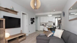 A modern living room with a grey sectional sofa, a wooden entertainment unit, a flat-screen TV, and a dining area in the background. - Ocean Paradise 2 la Tejita (Intero appartamento, due camere e un bagno) (Granadilla de Abona)