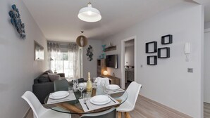 A modern dining area with a glass table, white chairs, and a chandelier. There is a sofa and a TV in the background. - Ocean Paradise 2 la Tejita (Intero appartamento, due camere e un bagno) (Granadilla de Abona)