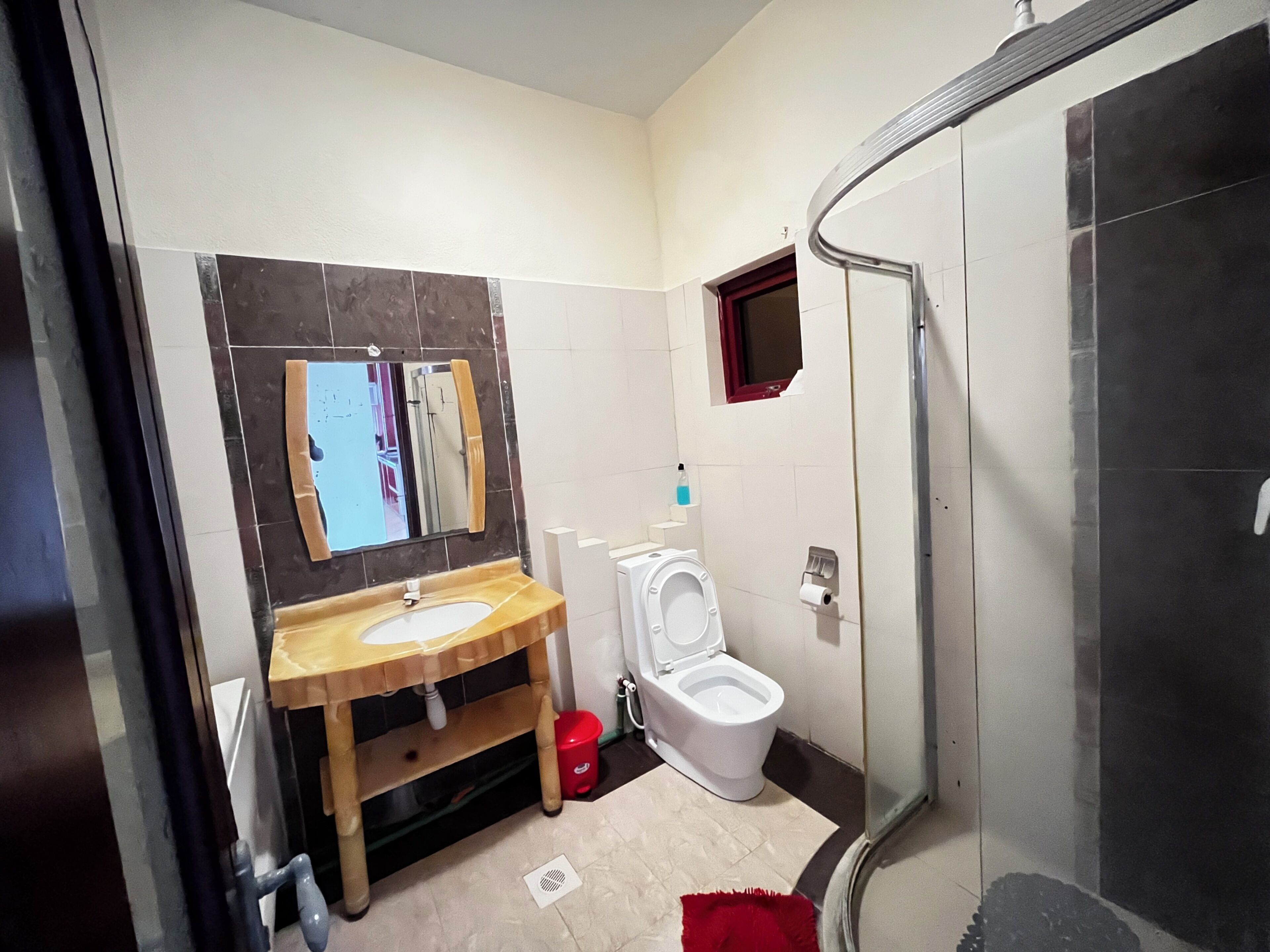 A bathroom with a wooden vanity, a white toilet, a shower area, and a mirror.
