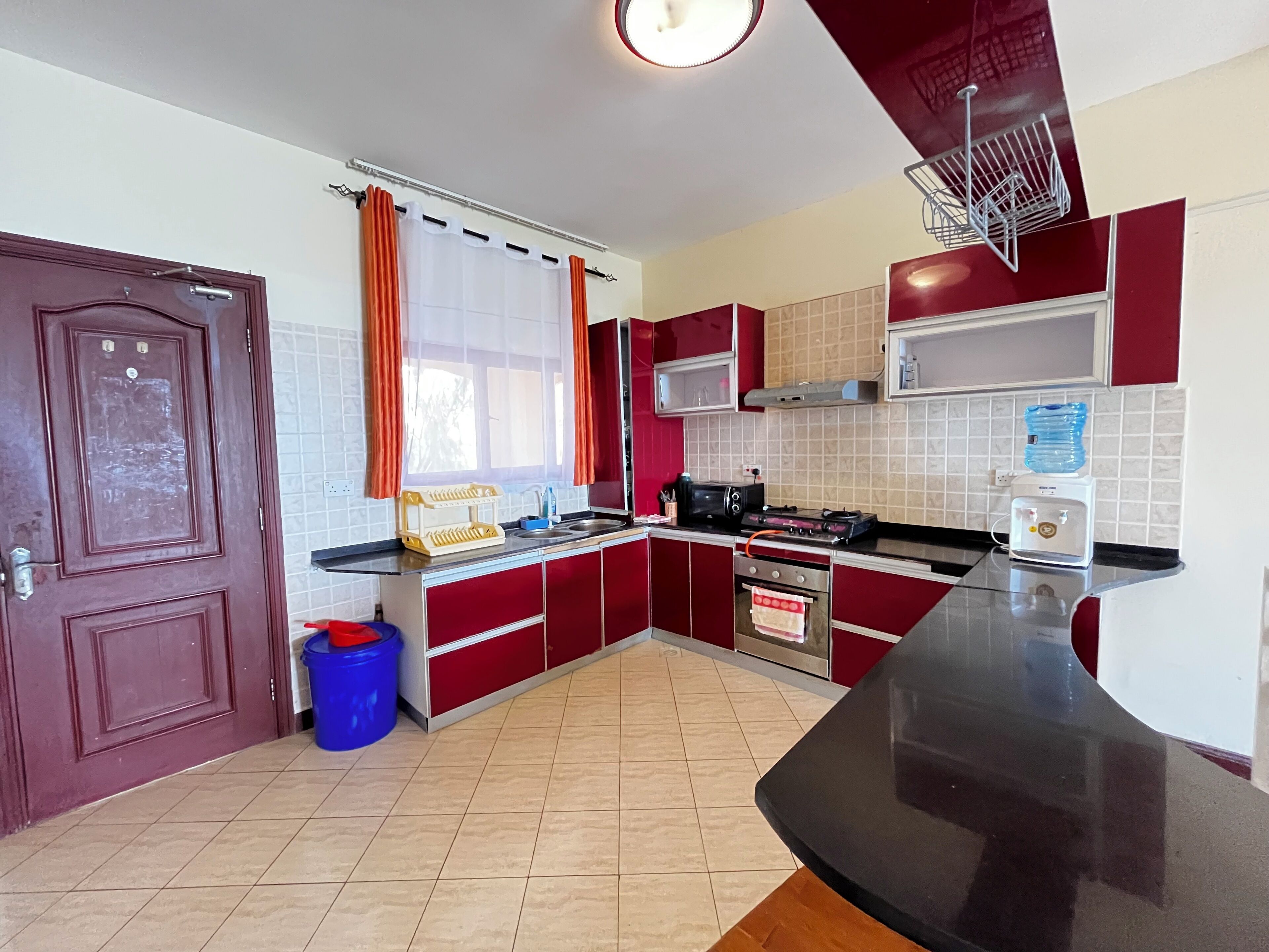Una cocina con gabinetes rojos, encimera negra, estufa, microondas y dispensador de agua.
