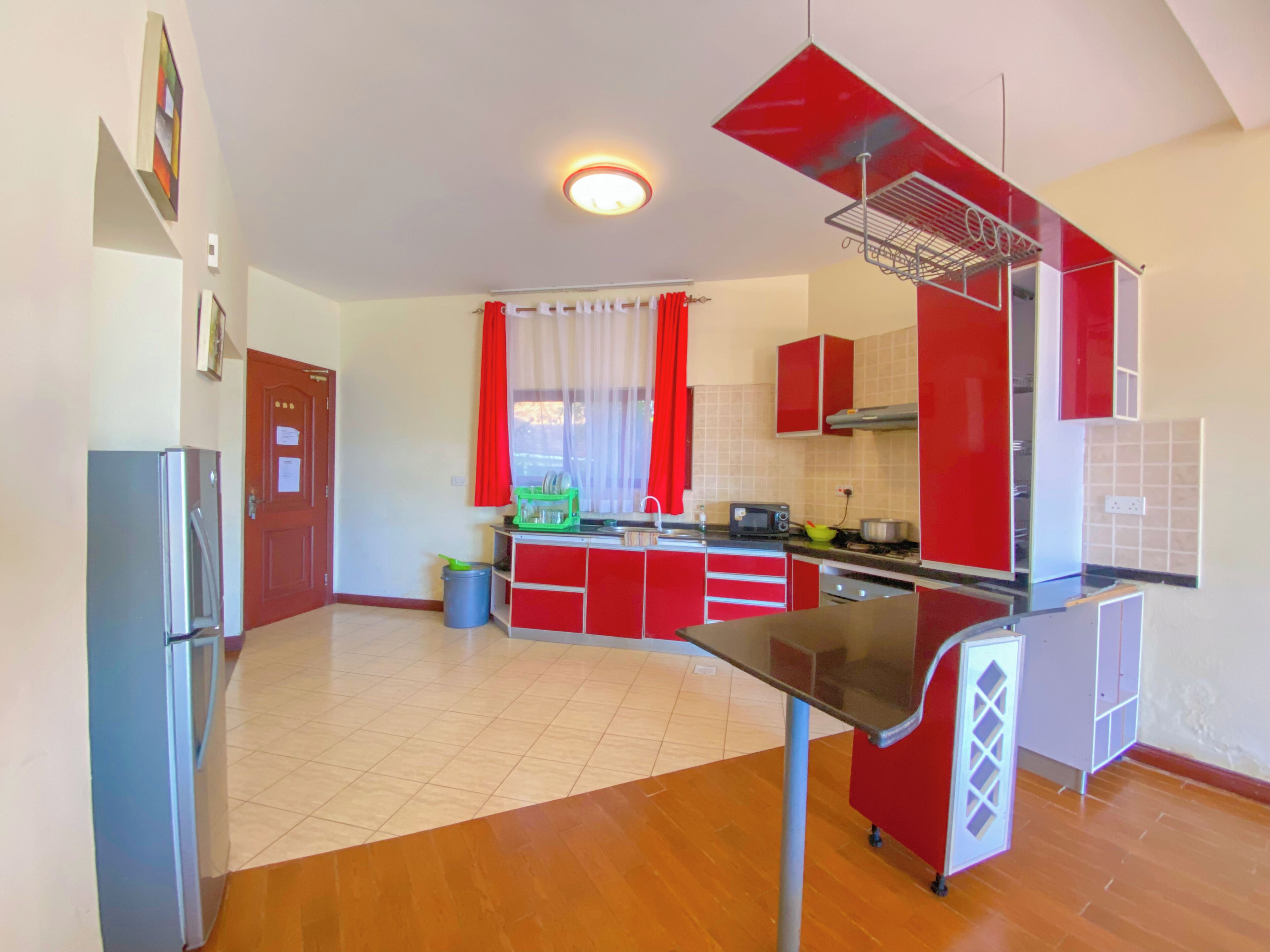 A modern kitchen with red cabinets, a stainless steel refrigerator, and a wooden floor.