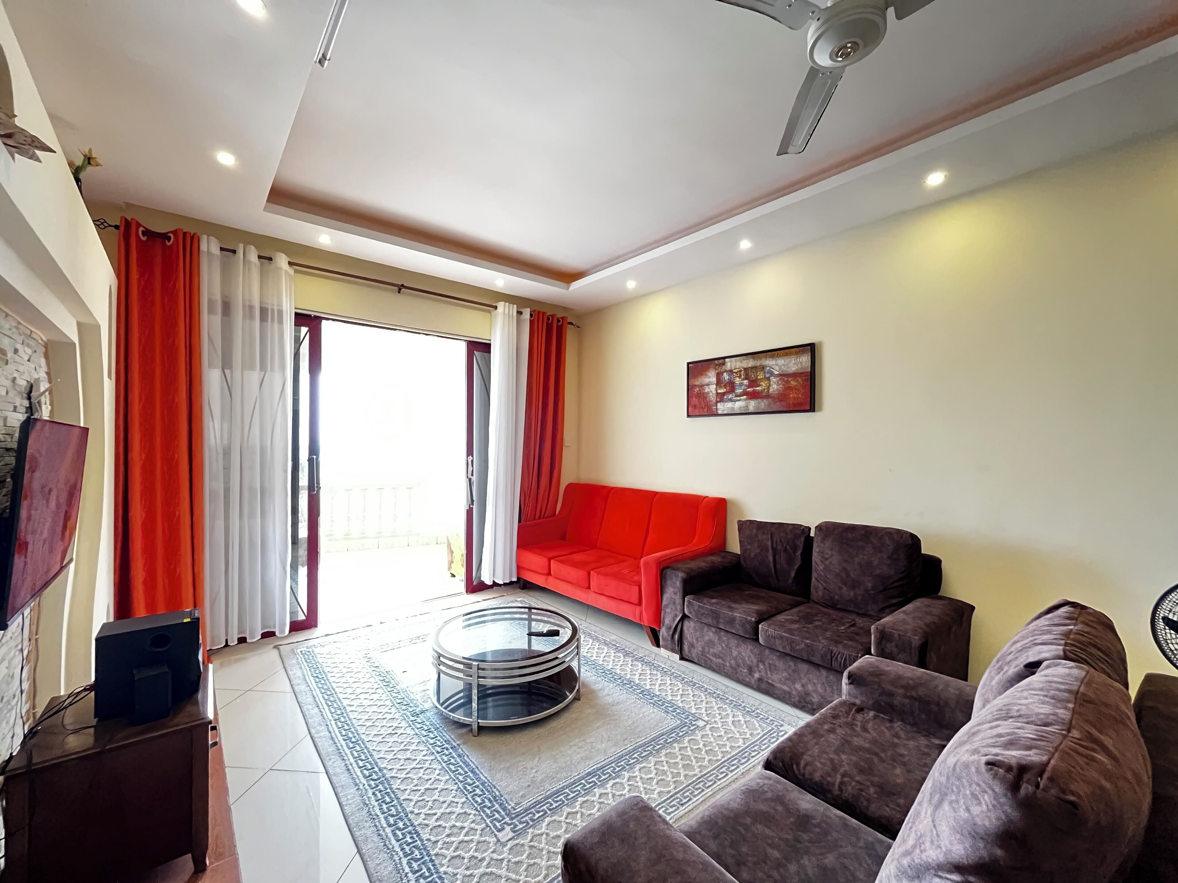 A living room with a red sofa, a brown sofa, a glass coffee table, and a ceiling fan.