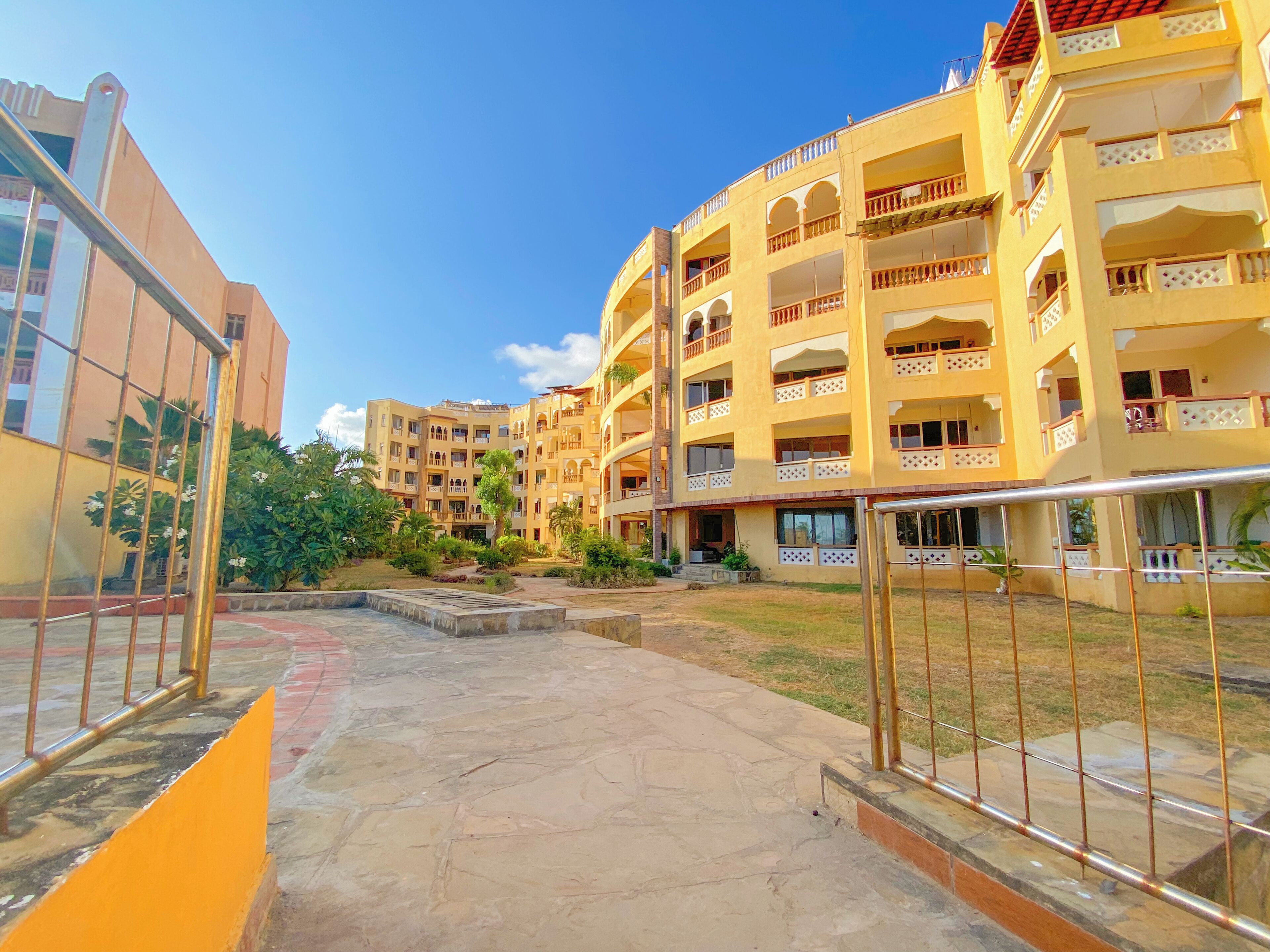 A courtyard with a stone floor, surrounded by yellow buildings with balconies and windows.