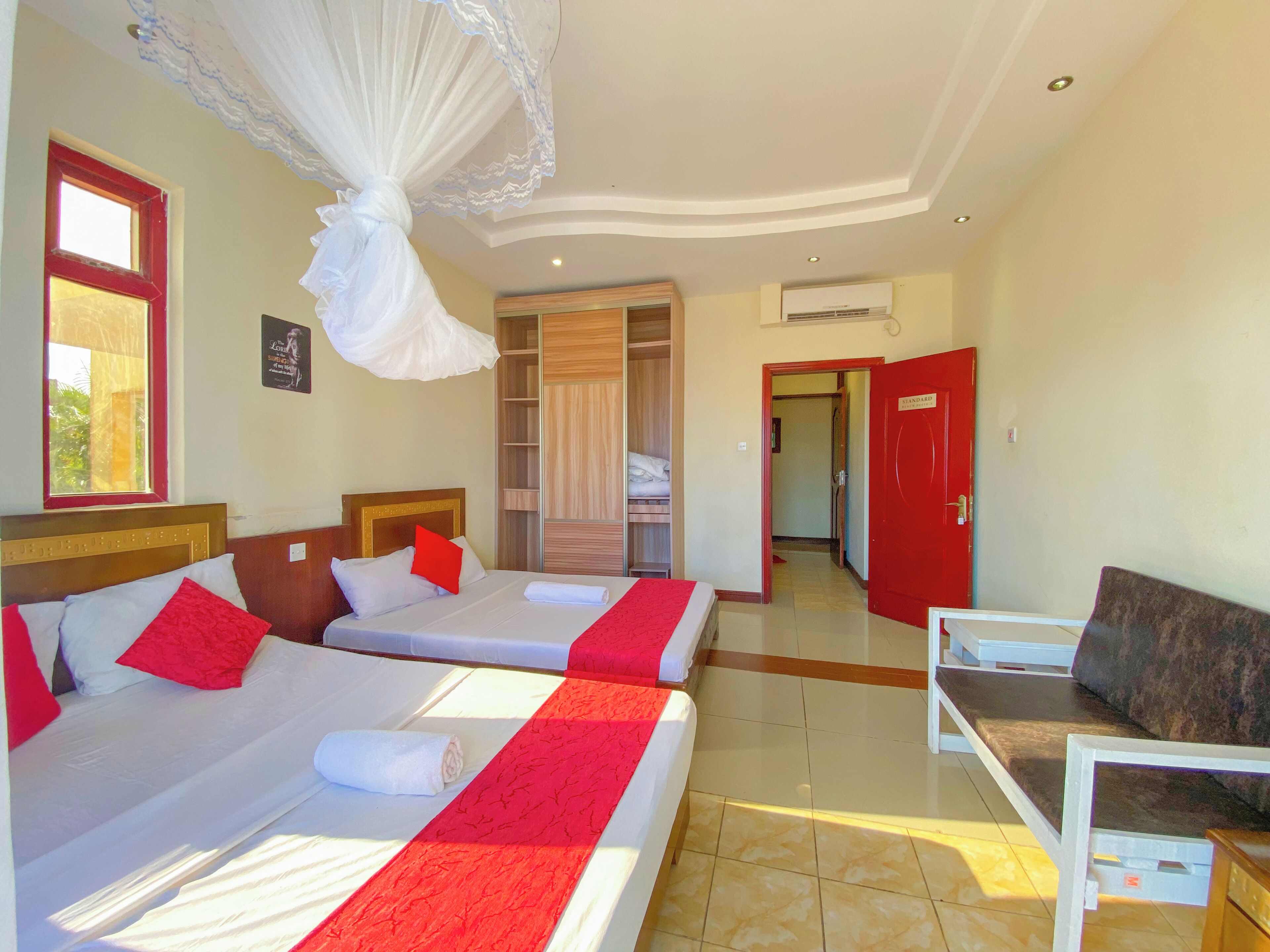 A hotel room with two beds, a TV, a wardrobe, and a bathroom visible through an open door.