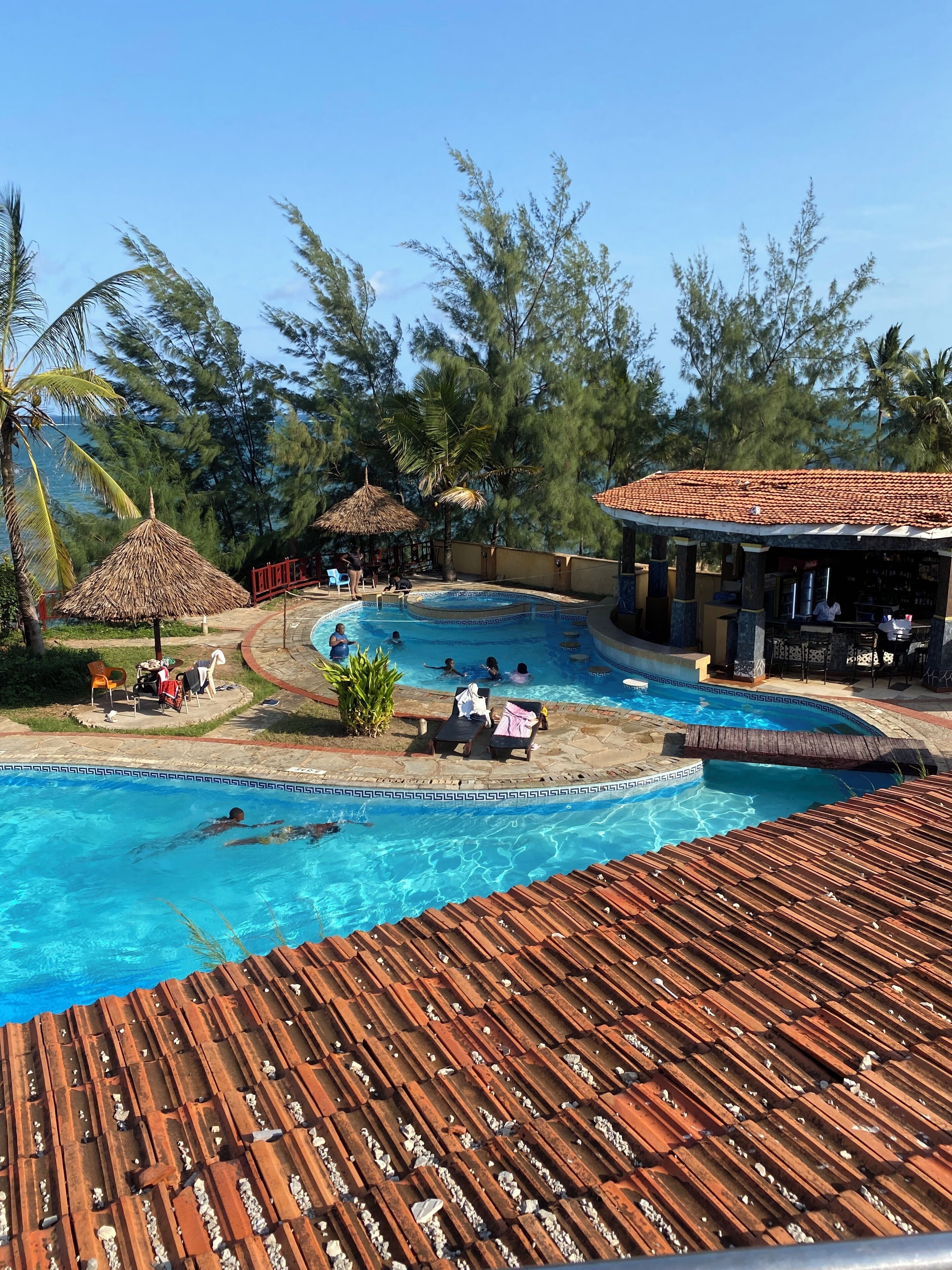 A swimming pool with lounge chairs and umbrellas, surrounded by trees and a building with a tiled roof.