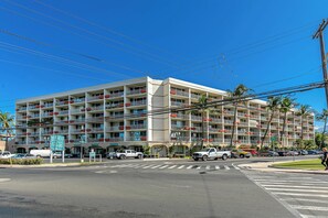 A multi-story hotel with balconies, a parking area, and a clear blue sky.