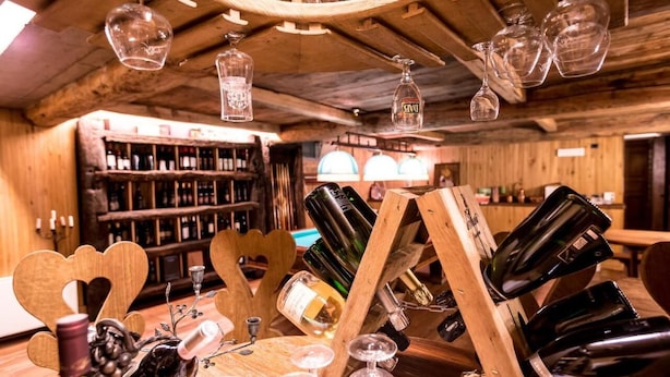 A rustic bar area with wooden shelves stocked with bottles, a wooden wine rack with bottles, and hanging glassware. - Hotel Lyshaus di Gressoney Saint Jean (Gressoney-Saint-Jean)
