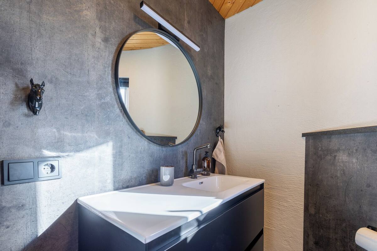 A modern bathroom with a large mirror, a white sink, and a towel rack.