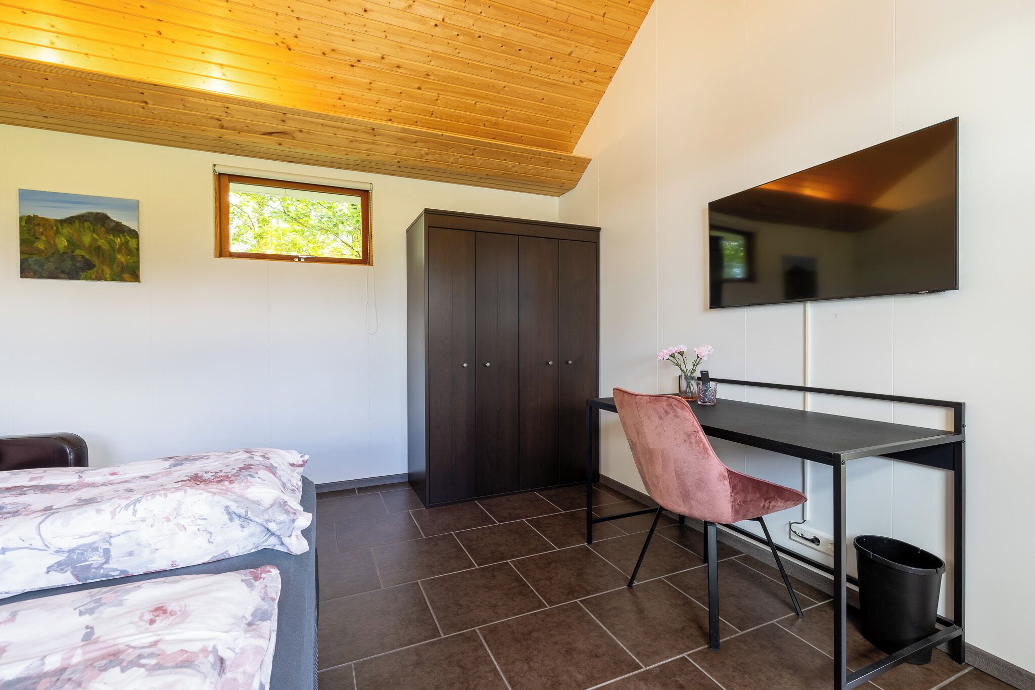 A bedroom with a bed, a desk with a chair, a wardrobe, a TV, and a window.