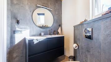 Un baño moderno con un espejo redondo, muebles oscuros y un inodoro a la vista.