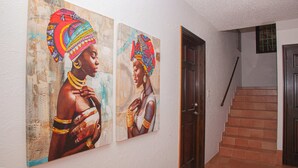 A hallway with two large paintings of a woman in traditional attire on the wall, a wooden door, and a staircase with brown tiles. - Beautiful spacious Studio with spectacular view (cole bay)