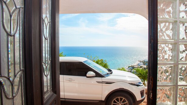 A white SUV parked in a covered area with a view of the ocean. - Beautiful spacious Studio with spectacular view (cole bay)