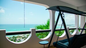 A balcony with a swing chair, a small table, and a view of the ocean and a coastal town. - Beautiful spacious Studio with spectacular view (cole bay)