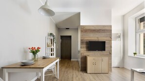 Een moderne keuken met een houten wandpaneel, een eethoek met een witte tafel en stoelen, en een televisie boven een houten kast.