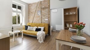 Een moderne woonkamer met een bakstenen muur, een gele bank, een houten tafel en een boekenkast met de tekst 'HOME'.